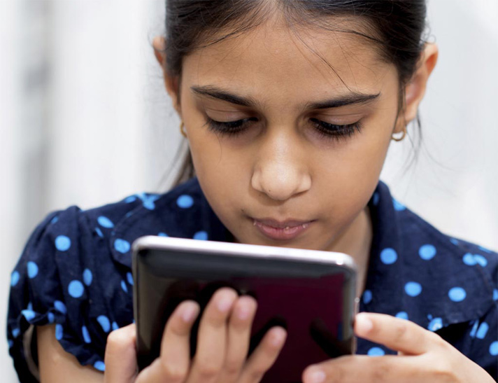 A girl with light brown skin and a ponytail looks down at a tablet.